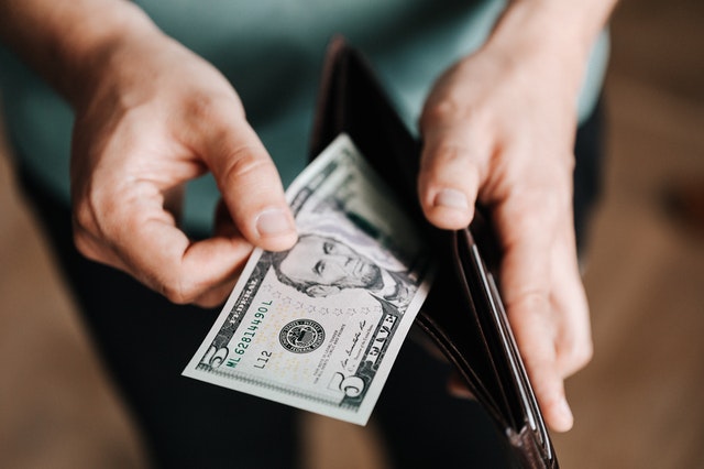 Person holding a wallet and pulling a five dollar bill out of it